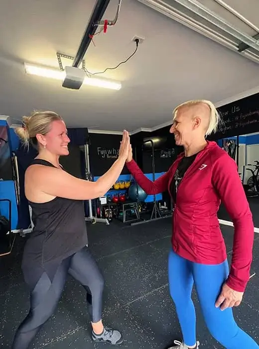 Two women in a gym, highlighting a supportive moment between a client and female personal trainer